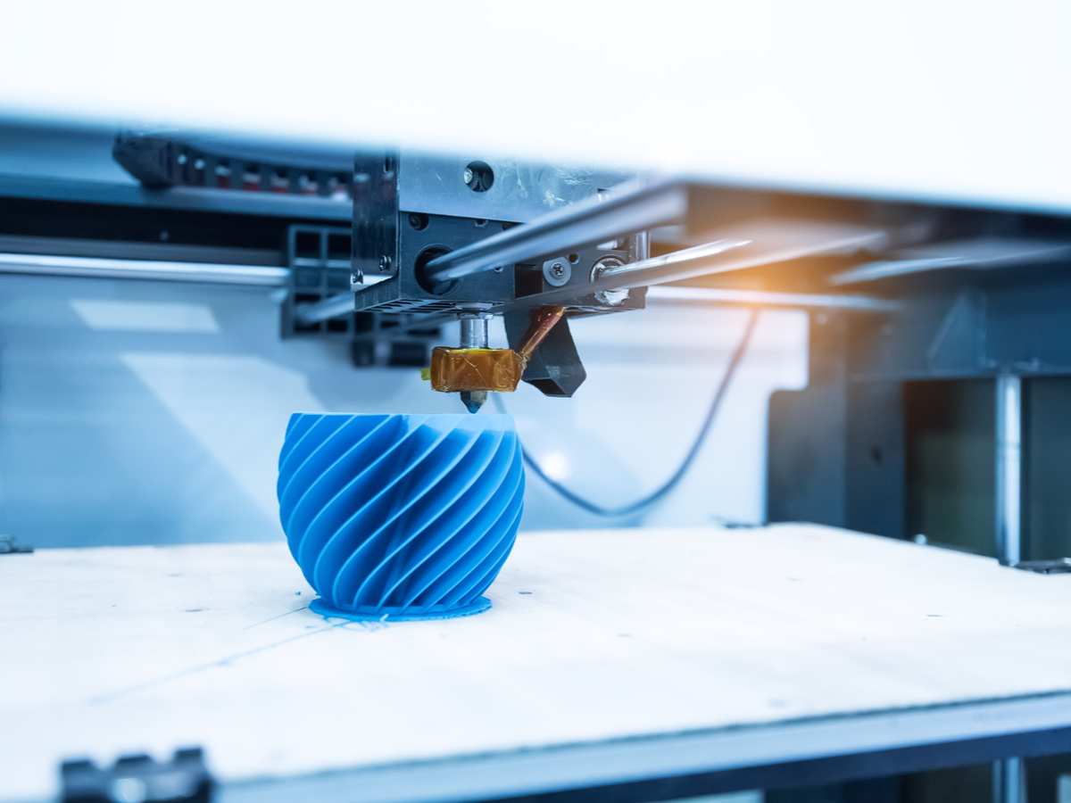 3D printing machine in the process of printing a solid blue, spiraled object which sits on a platform.