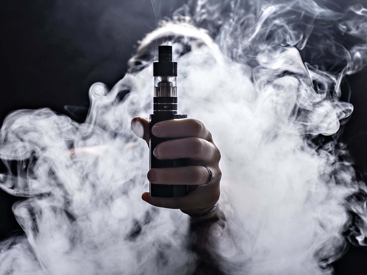 Hand with ring holding a vaporizer our towards the viewer. Cloud of smoke encircles wrist and obscures view of the person.