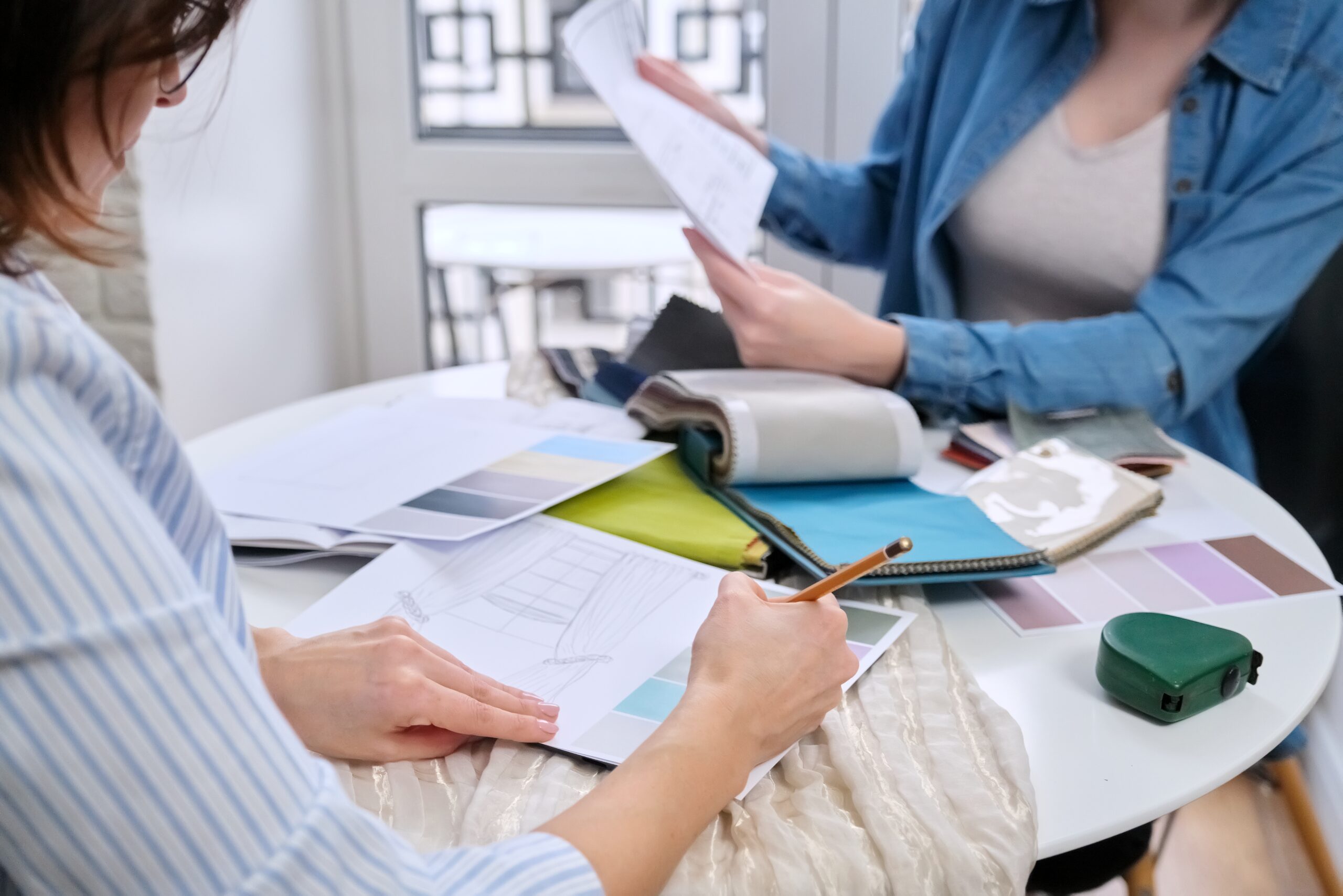 Interior design, two working colleagues designers, or decorator and client choosing curtain fabrics, women looking at samples discussing curtain models