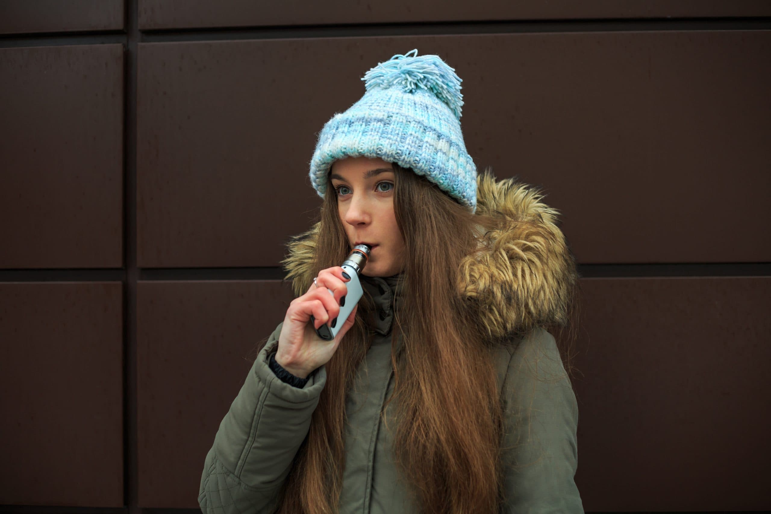 Female teenager in winter clothing, vaping outside