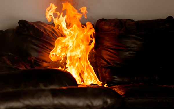 Small fire on seat cushion of brown leather sofa.