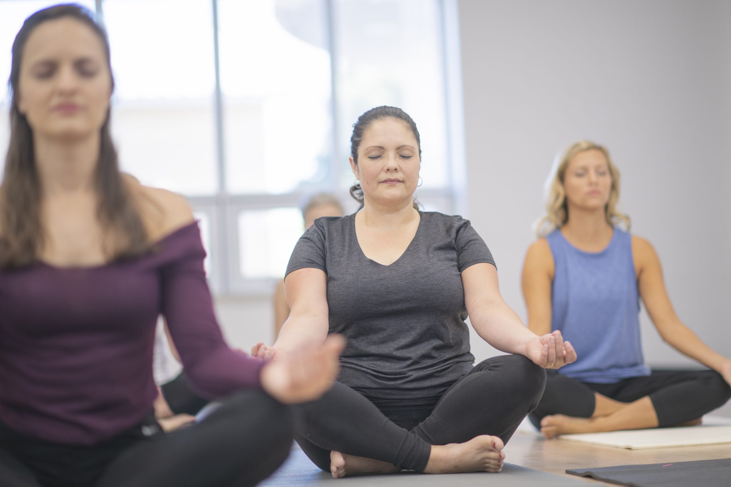 Group of women in yoga class with eyes closed, cross-legged and hands on knees.